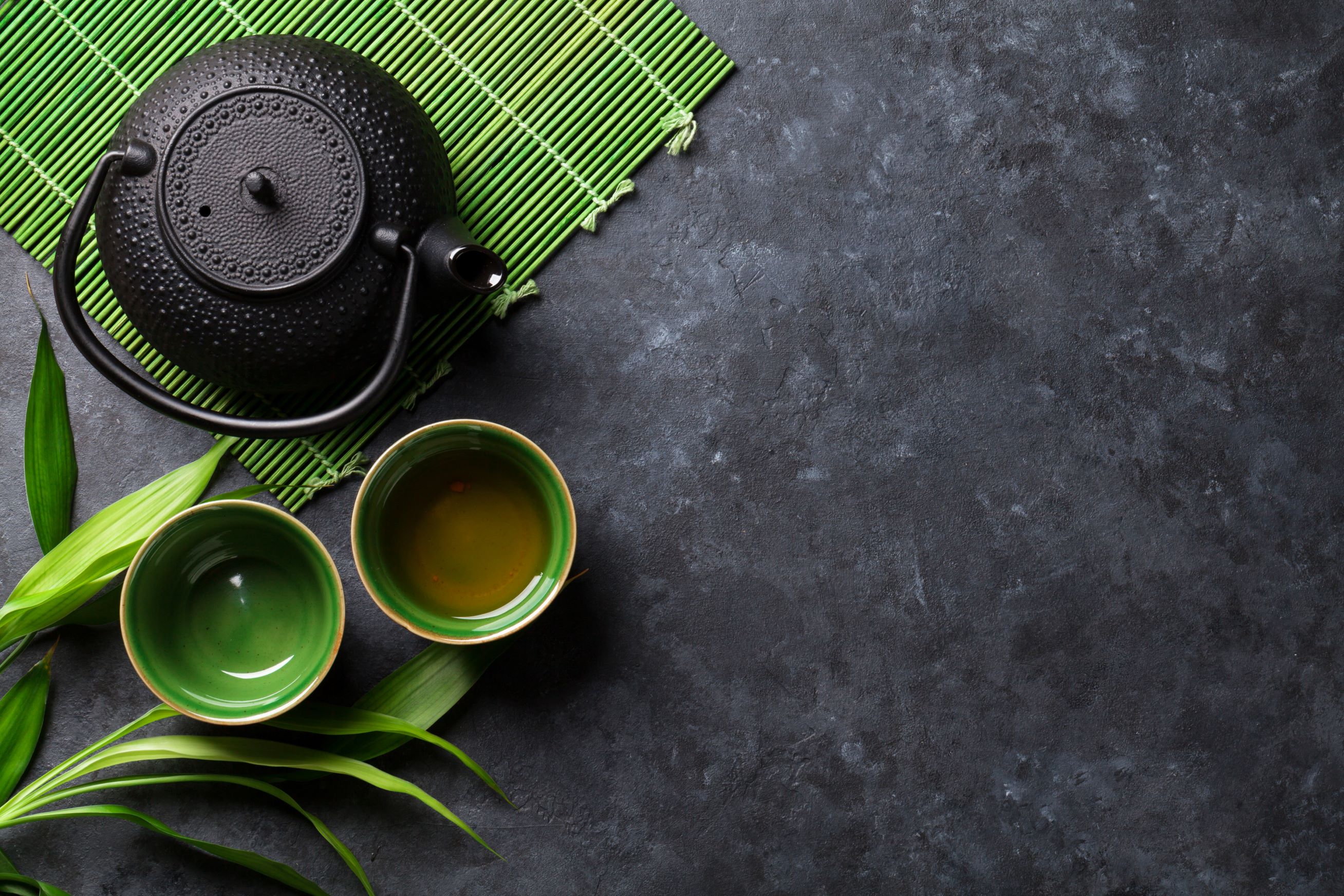 Cup of green and black tea next to black tea-pot