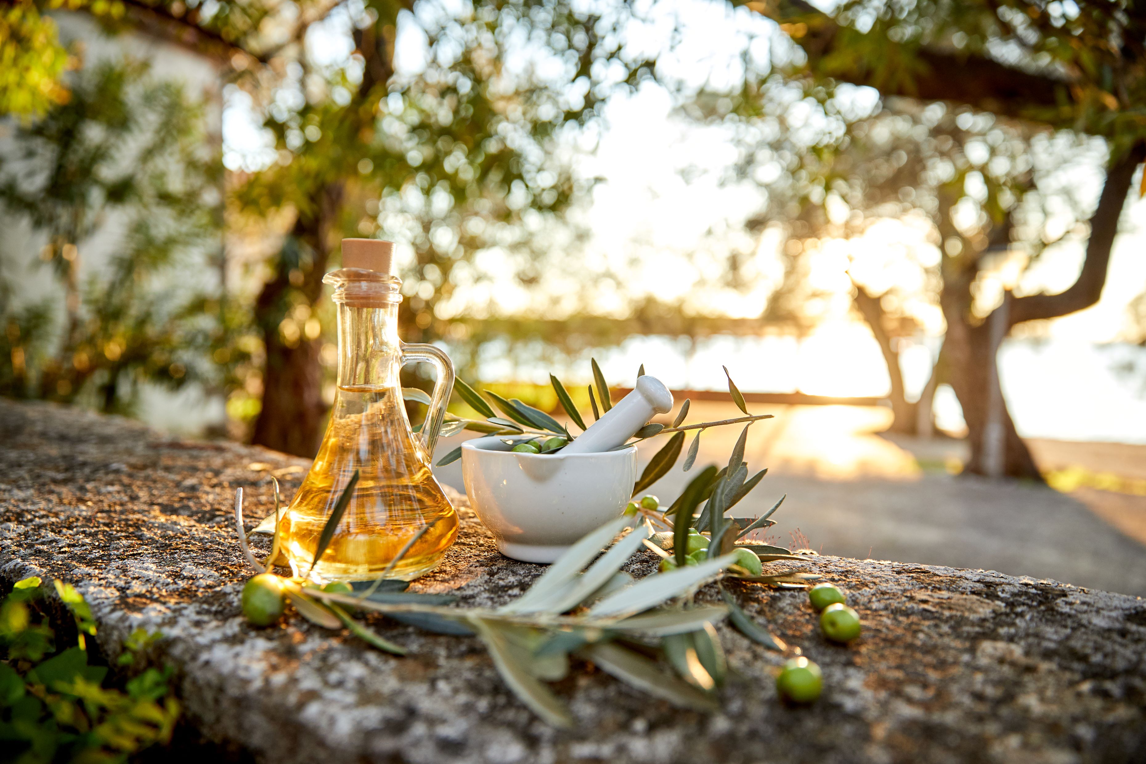 Olives and bottle of olive oil on stone wall with sunlit olive grove in background