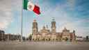 Mexican flag in foreground, in front of the historic Plaza Zócalo in Mexico City