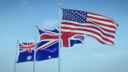 Flags of UK, US and Australia flying from flagpoles against a calm blue sky 